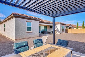 Un patio cubierto con una mesa y sillas, un pequeño edificio con techo de tejas y suelo de grava.