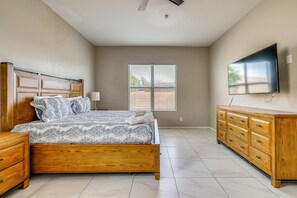 Un dormitorio con una cama de madera, un aparador, un televisor en la pared y una ventana con persianas.