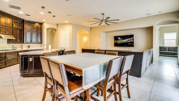 A modern kitchen with dark wooden cabinets, a central island, and a dining area with a large table and chairs. - 'Rapt Expression' Queen Creek Home w/ Patio! (Queen Creek)