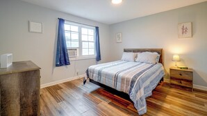 Un dormitorio con cama, una mesita de noche con lámpara, una ventana con cortinas y un aire acondicionado instalado en la pared.