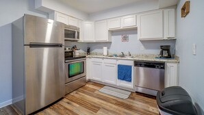 Una cocina compacta con gabinetes blancos, electrodomésticos de acero inoxidable y piso de madera.