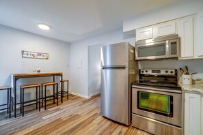 Eine Küche mit einem Edelstahl-Kühlschrank, einer Mikrowelle und einem Backofen. Es gibt Holzschemeln und einen kleinen Tisch.