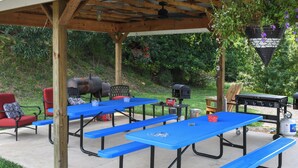 An outdoor patio with picnic tables, a barbecue grill, and a seating area.