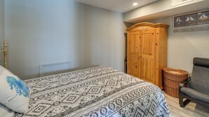 A bedroom with a bed, a wardrobe, a chair, and a wall-mounted shelf with decorative items.