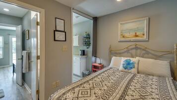 A bedroom with a bed, a nightstand, a painting, and a bathroom visible through an open door.