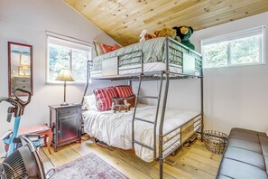 Una cama litera con un espejo, una lámpara y un pequeño aparador en una habitación con suelo de madera y ventanas.