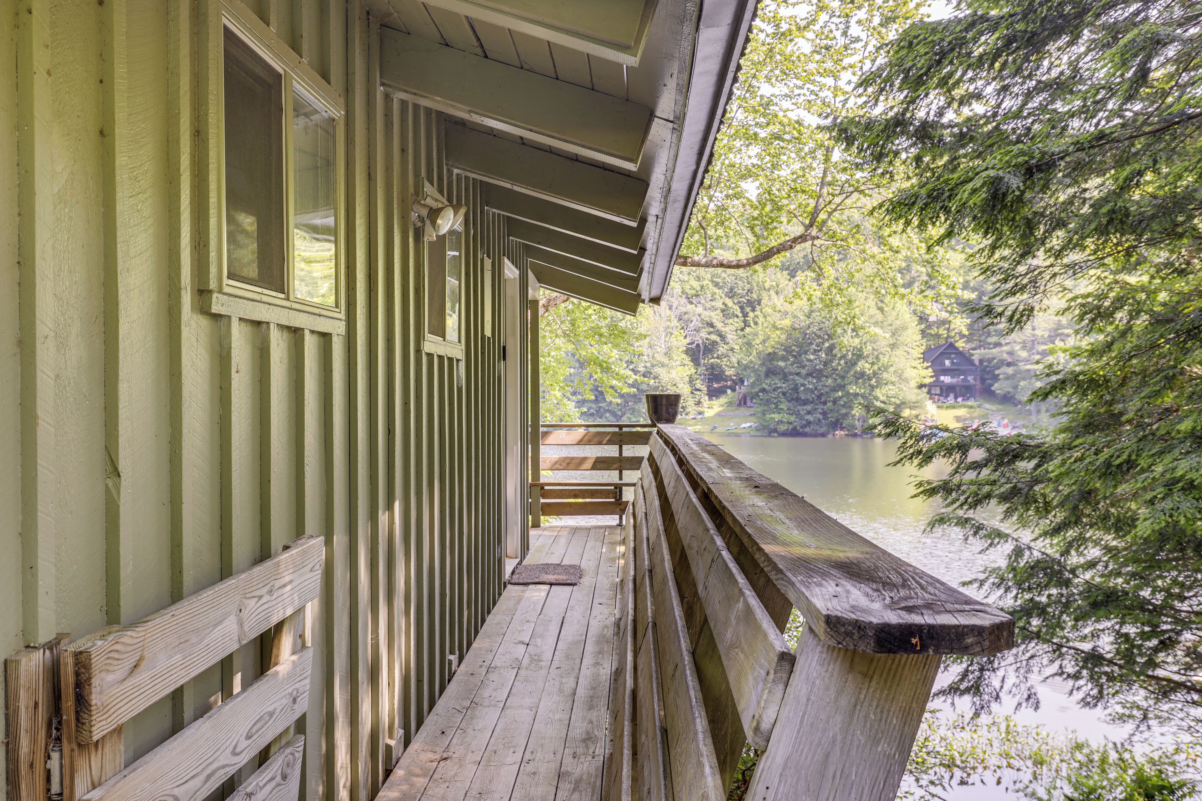 A wooden deck with a railing overlooking a calm lake, surrounded by trees.