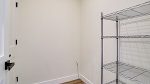 A corner of a room with a white wall, a wooden floor, and a metal shelving unit against the wall. - Updated Family Home w/ Patio in Brighton (Brighton)
