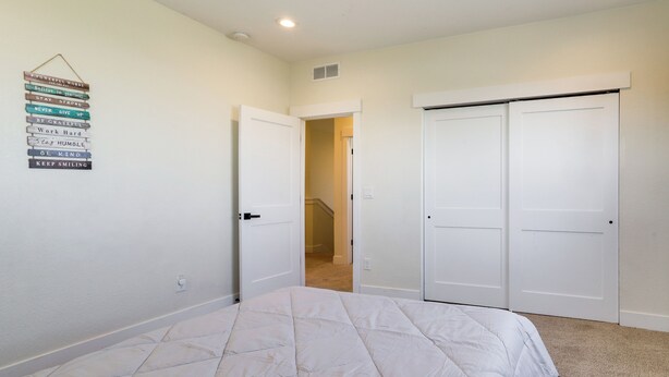 A bedroom with a bed, a wall-mounted motivational quote, a white door, and a closet. - Updated Family Home w/ Patio in Brighton (Brighton)