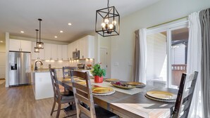 A modern kitchen with white cabinets, a stainless steel refrigerator, and a dining area with wooden chairs and a table set for four. - Updated Family Home w/ Patio in Brighton (Brighton)