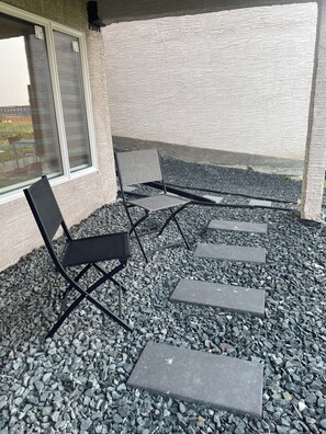 Een terras met twee stoelen en een tafel, omgeven door een grindpad en een gebouw met een structuurwand.
