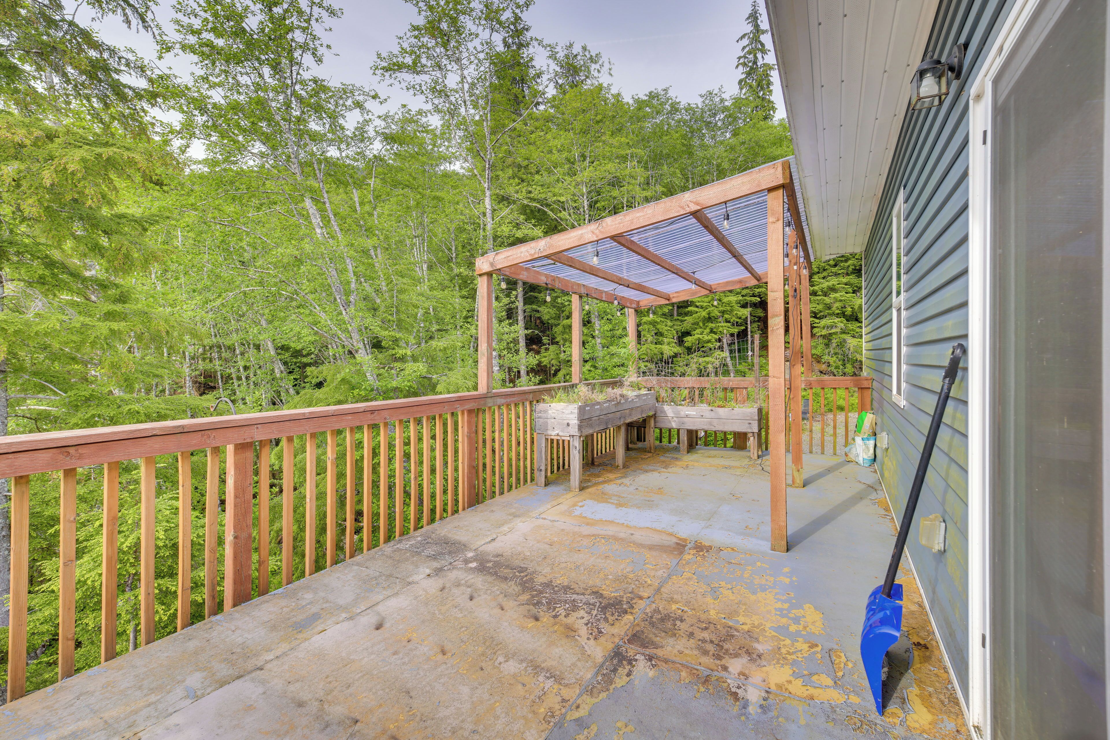 Una terraza de madera con pérgola, piso de concreto y vista a un área boscosa.