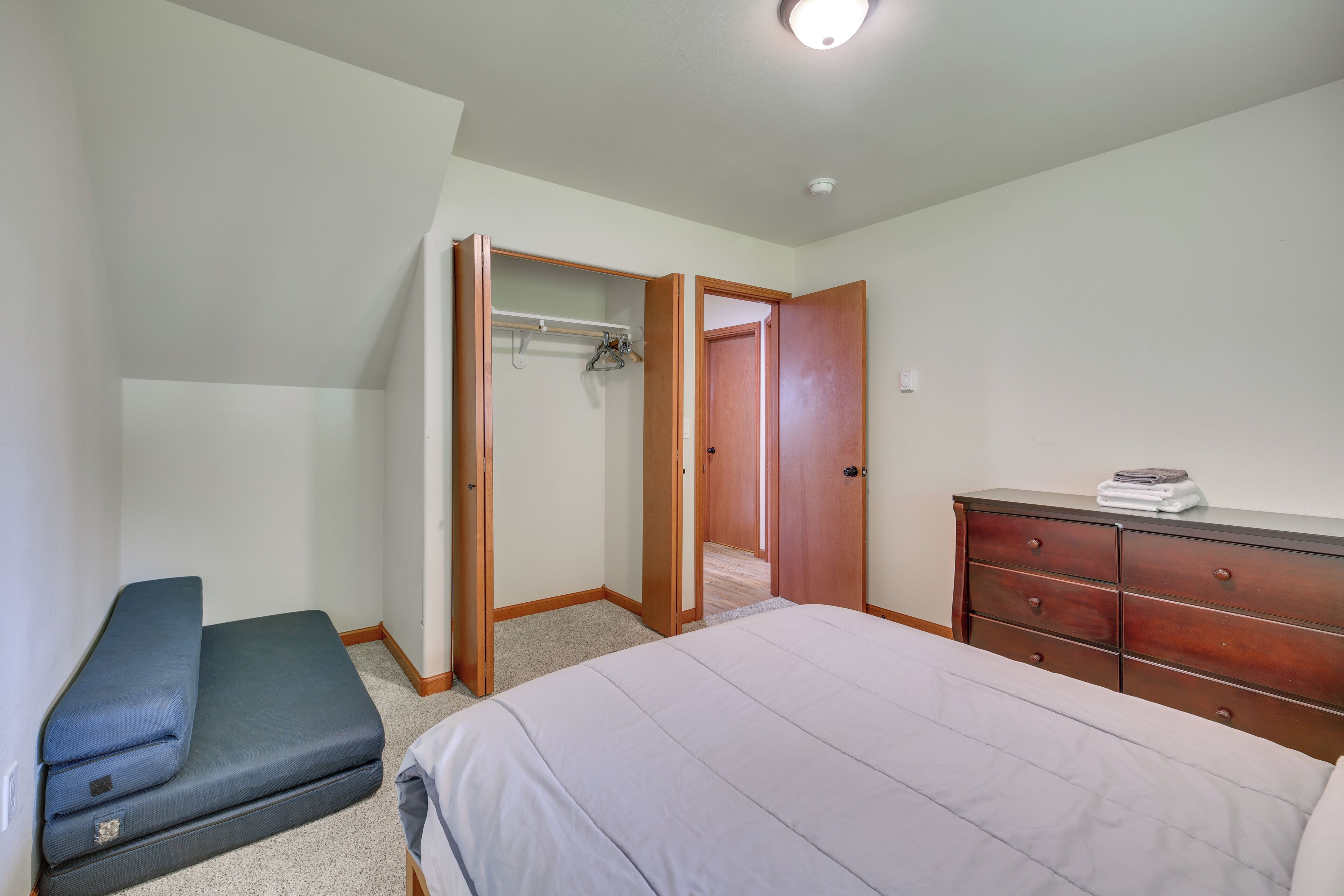 A bedroom with a bed, a dresser, a bench, and an open closet.