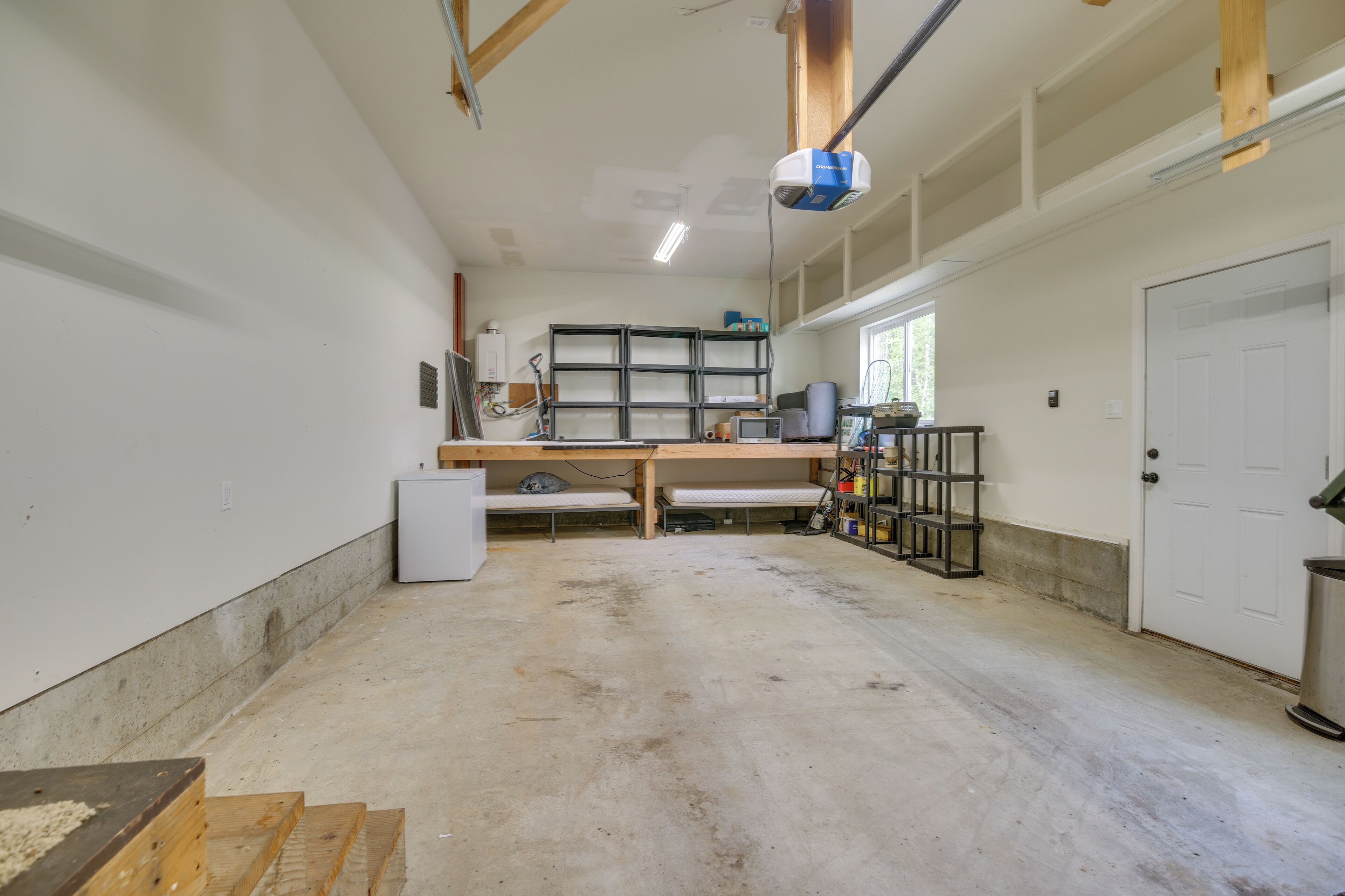 A spacious room with a large workbench, shelving units, and a door.