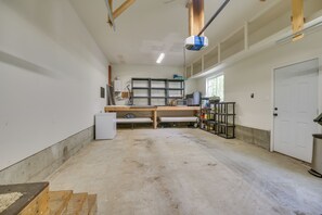 A spacious room with a large workbench, shelving units, and a door.