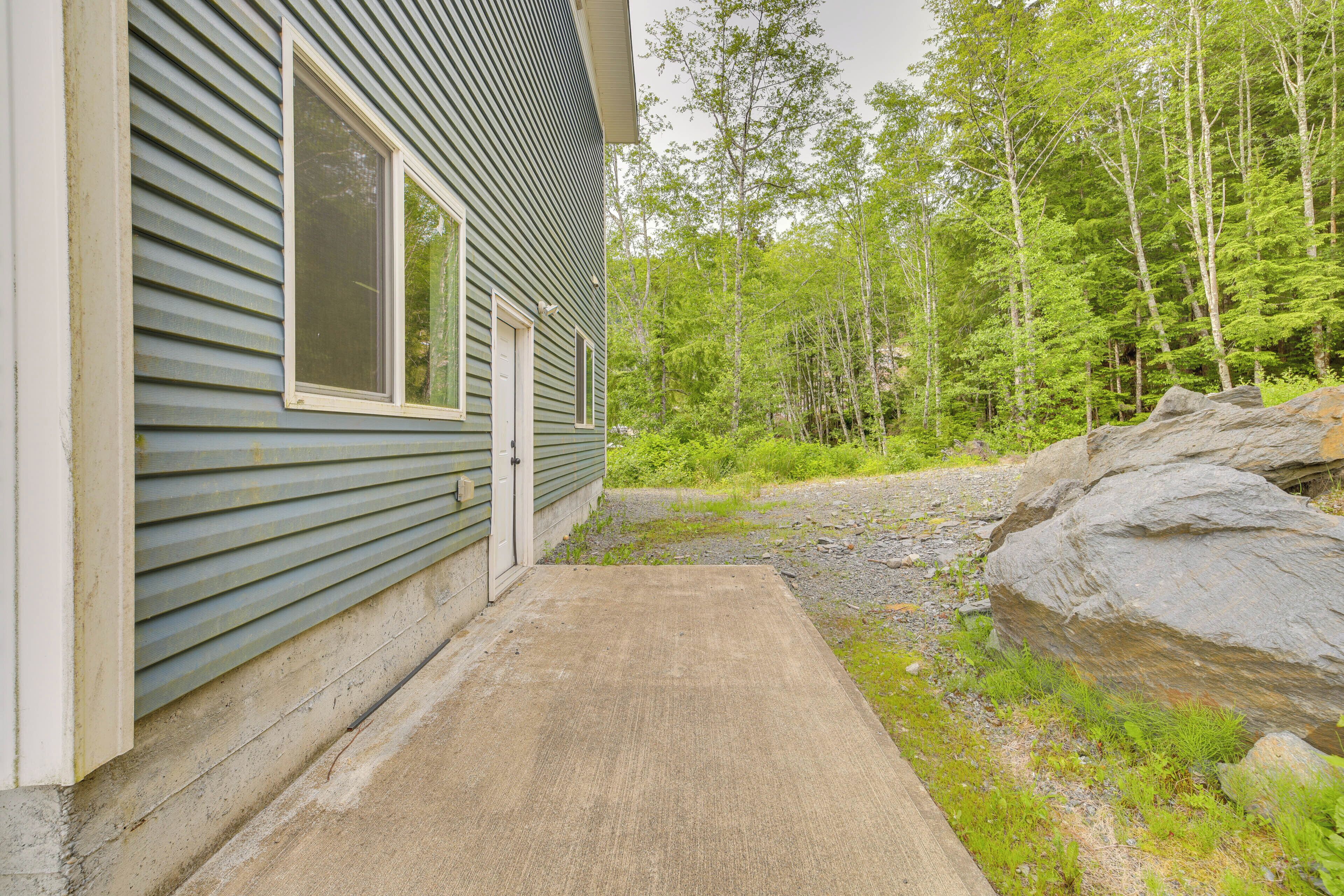 A house with a concrete pathway leading to the entrance, surrounded by a forested area and large rocks.