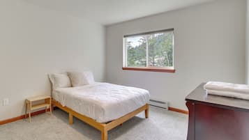 A bedroom with a bed, a small wooden nightstand, a window with a view of trees, and a dark wooden dresser.