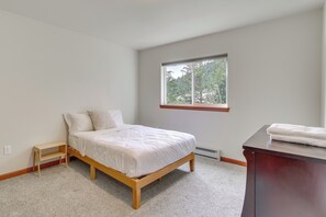 A bedroom with a bed, a small wooden nightstand, a window with a view of trees, and a dark wooden dresser.