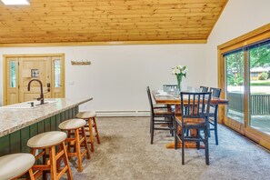 A kitchen with a wooden ceiling, a bar area with stools, a dining table with chairs, and a view through large windows. - Near Beach & Trails! Lake Winnipesaukee Cabin (Moultonborough)
