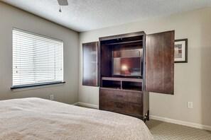 Une chambre avec un grand lit, une armoire dont les portes sont ouvertes, une fenêtre avec des stores et un tableau accroché au mur.