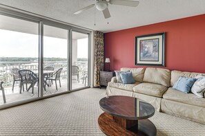 A room with a sofa, a glass coffee table, and a view of a balcony with chairs. - Tee Times & Pool Vibes! North Myrtle Beach Retreat (North Myrtle Beach)