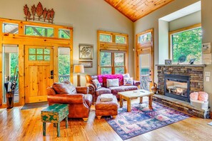 Ein gemütliches Wohnzimmer mit Ledersofas, einem Kamin und großen Fenstern mit Blick auf Grünflächen.