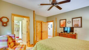 Quarto com cama, televisão, relógio e ventoinha no teto.