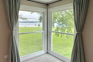 Une chambre d’angle avec deux fenêtres donnant sur un espace verdoyant et une étendue d’eau.