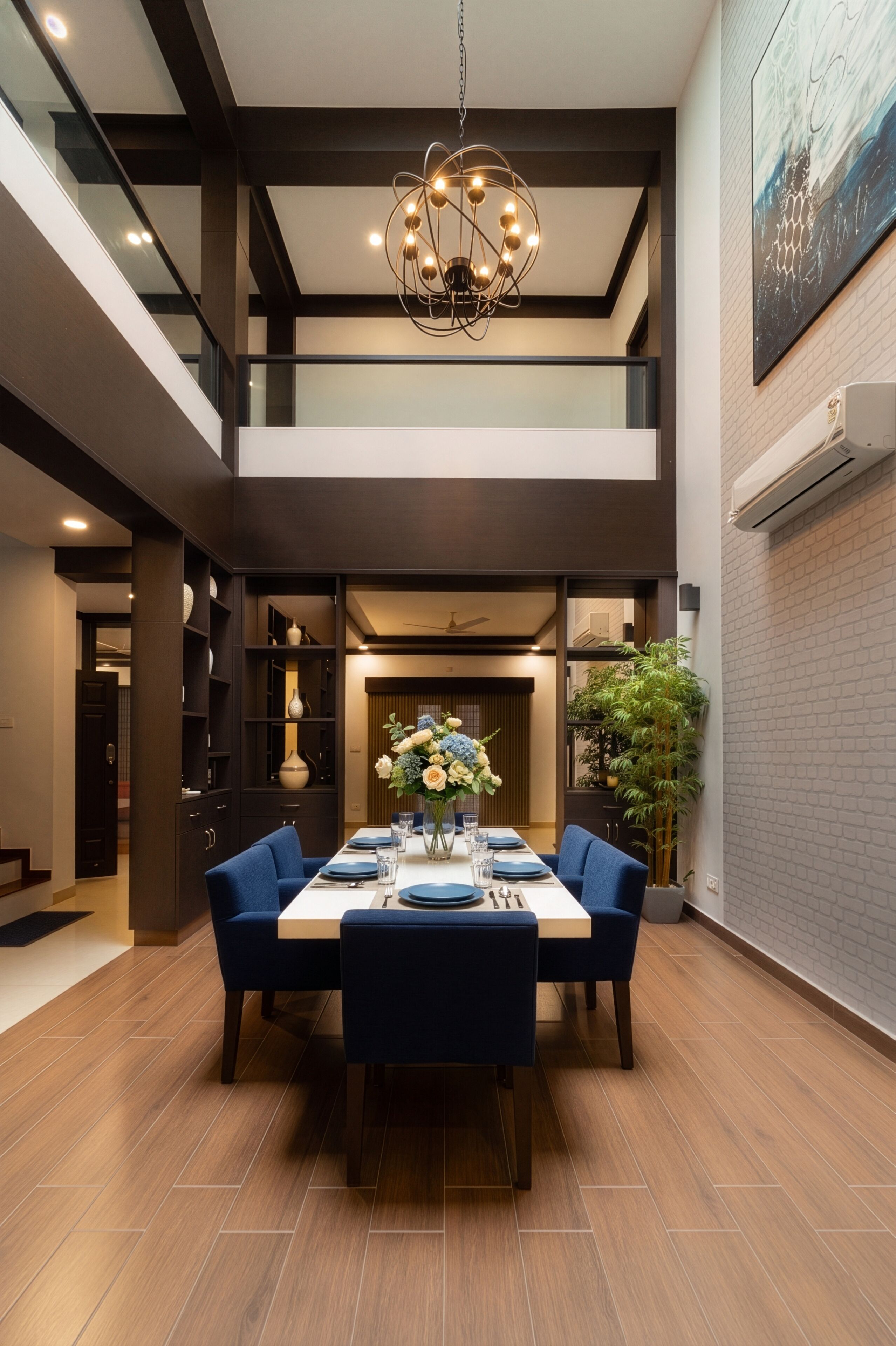 Uma sala de jantar moderna com teto alto, um candelabro e uma mesa posta para quatro pessoas.