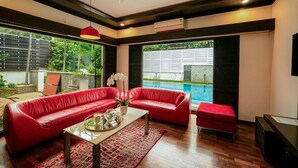 A modern living room with a red sofa set, a coffee table, and a view of a swimming pool. - ELIVAAS Gerrys 4BHK Villa with Terrace (Chennai)