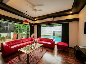 A modern living room with a red sofa set, a coffee table, and a view of a swimming pool.