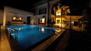 A swimming pool with a metal ladder, surrounded by a building with a balcony and a covered area. - ELIVAAS Gerrys 4BHK Villa with Terrace (Chennai)