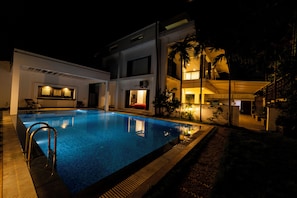 A swimming pool with a metal ladder, surrounded by a building with a balcony and a covered area.
