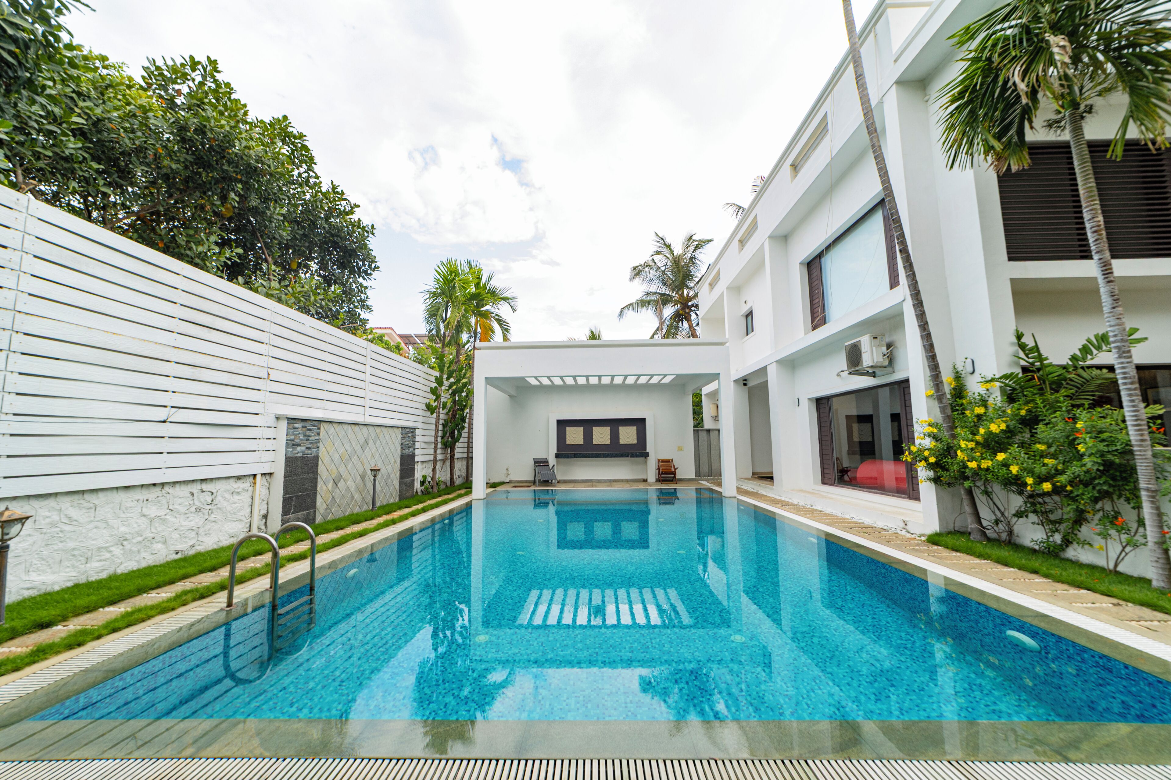 Une piscine à l’eau d’un bleu cristallin, entourée d’un bâtiment blanc doté d’un balcon et d’un palmier.