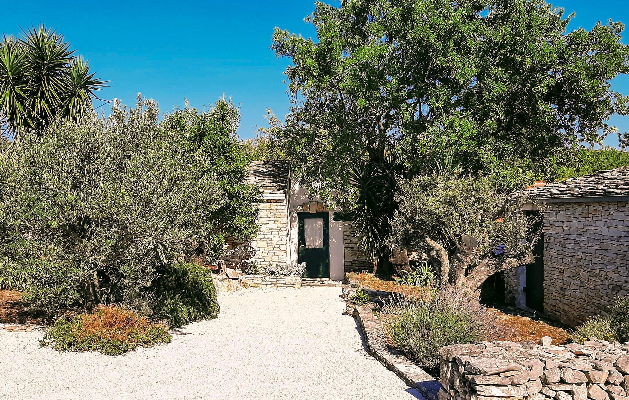 A stone building with a door, surrounded by dense vegetation and a gravel path leading to it.