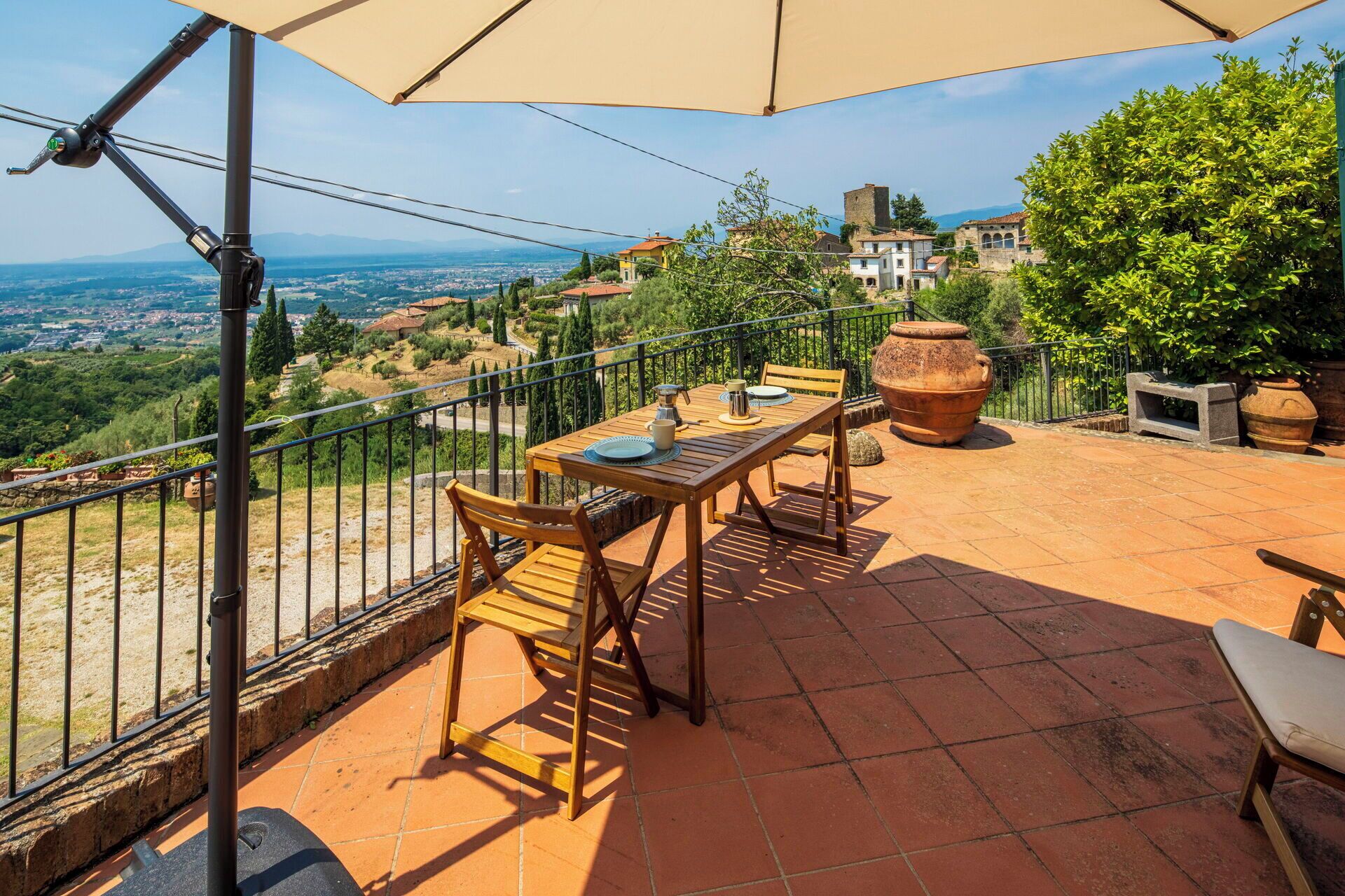 A terrace with a table and chairs, a large umbrella, and a view of a town.