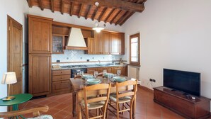 A kitchen with wooden cabinets, a dining table set with plates and glasses, a television, and a lamp. - Vacation Home in Lamporecchio with 1 bedrooms sleeps 4 (Lamporecchio)