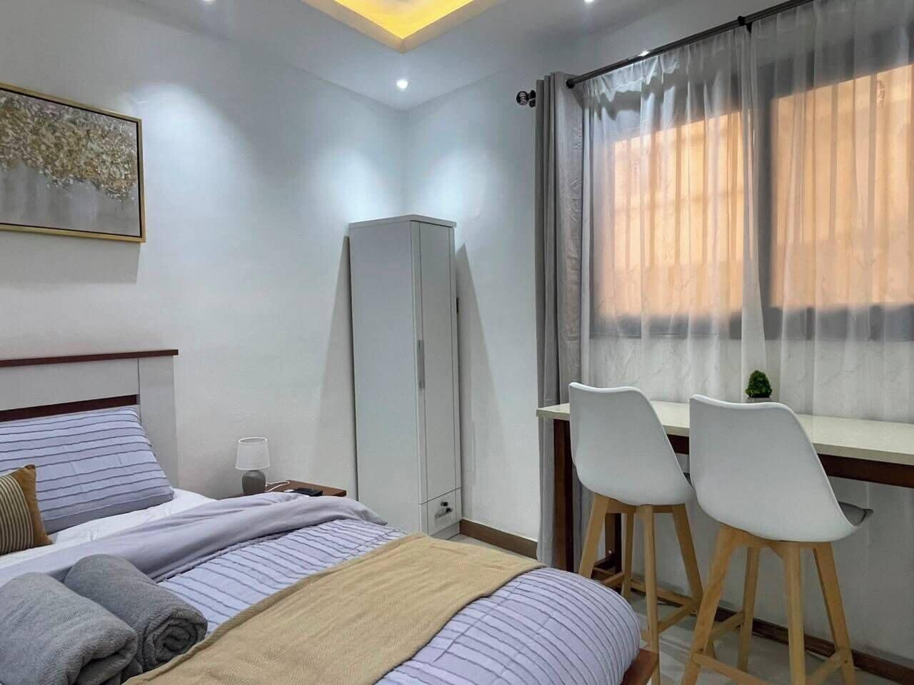 A bedroom with a bed, a desk, two chairs, a wardrobe, and a window with curtains.
