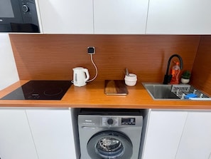 Une cuisine compacte équipée d’un lave-linge intégré, d’une machine à café et d’un évier.