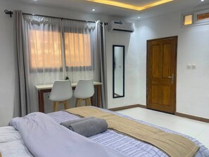 A bedroom with a bed, a desk with chairs, a mirror, and a wooden door. - Fully Equiped Modern Studio in Dakar (Dakar)