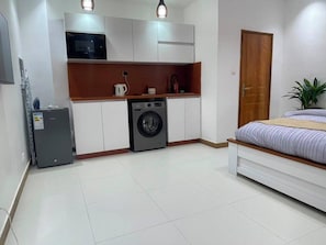 A compact room with a bed, a washing machine, a microwave, and a small cabinet. - Fully Equiped Modern Studio in Dakar (Dakar)