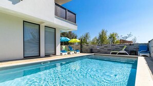 A modern outdoor swimming pool with clear blue water, surrounded by lounge chairs and umbrellas. - Beautiful apartment in Medulin with swimming pool (Medulin)