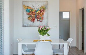 Ein Essbereich mit einem weißen Tisch, zwei Stühlen, einer Blumenvase und einem farbenfrohen Schmetterlingsbild an der Wand.