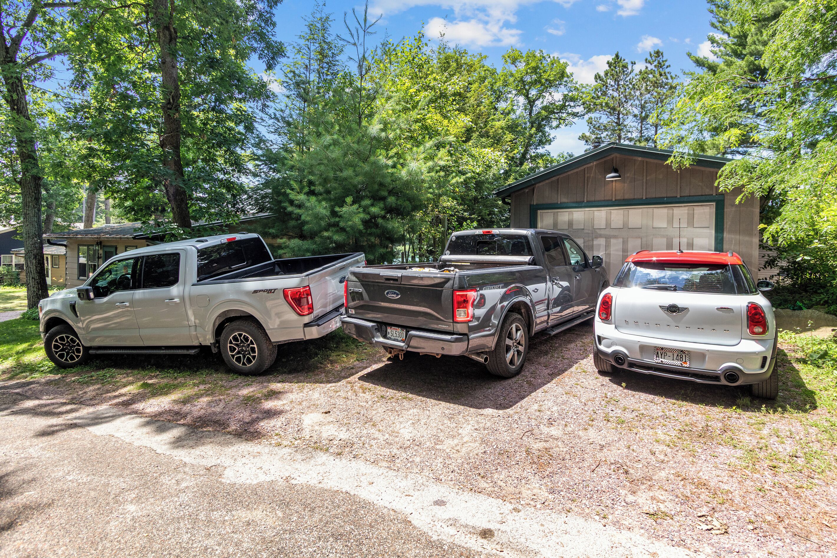 Tres vehicles de l'estil pickup estacionats a la entrada d'una casa, amb un garatge al fons.