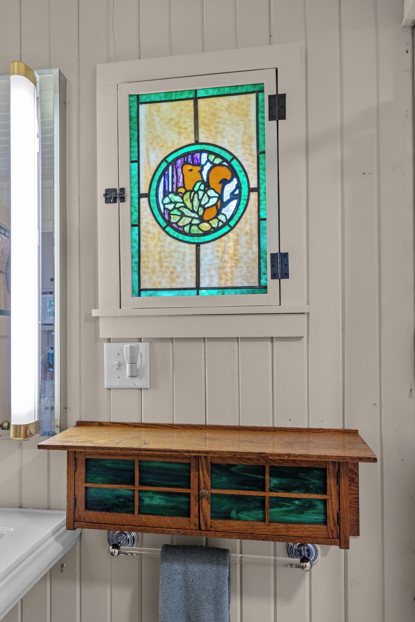 Un baño con tocador de madera, una ventana de vitral y un perchero.