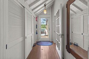 A hallway with a wooden floor, white doors, and a view of a backyard with a patio and a tree. - Waterfront Getaway | Fish, Paddle & Relax (Westfield)
