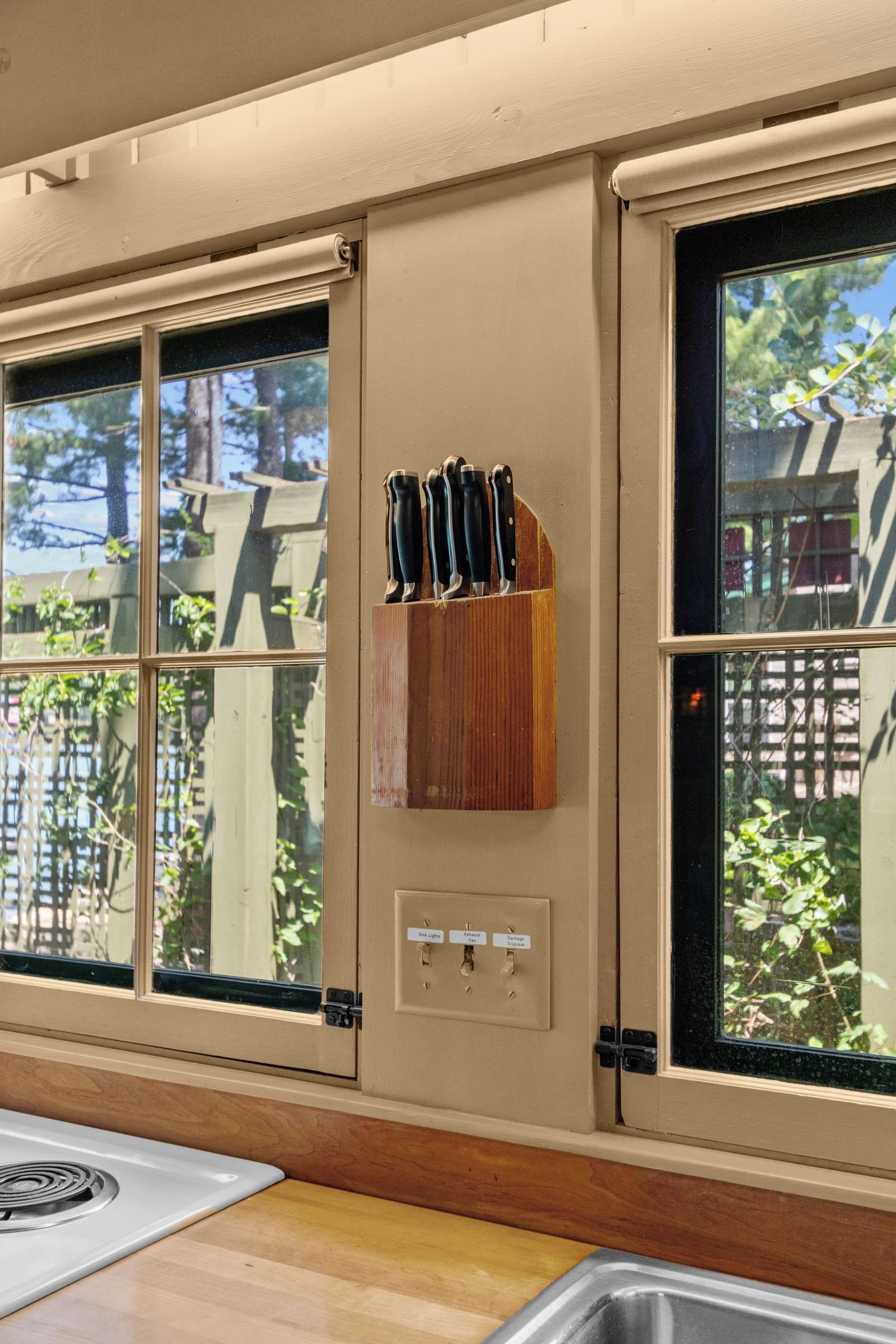 Une cuisine avec un plan de travail en bois, une cuisinière et une fenêtre sur laquelle est fixé un porte-couteaux.