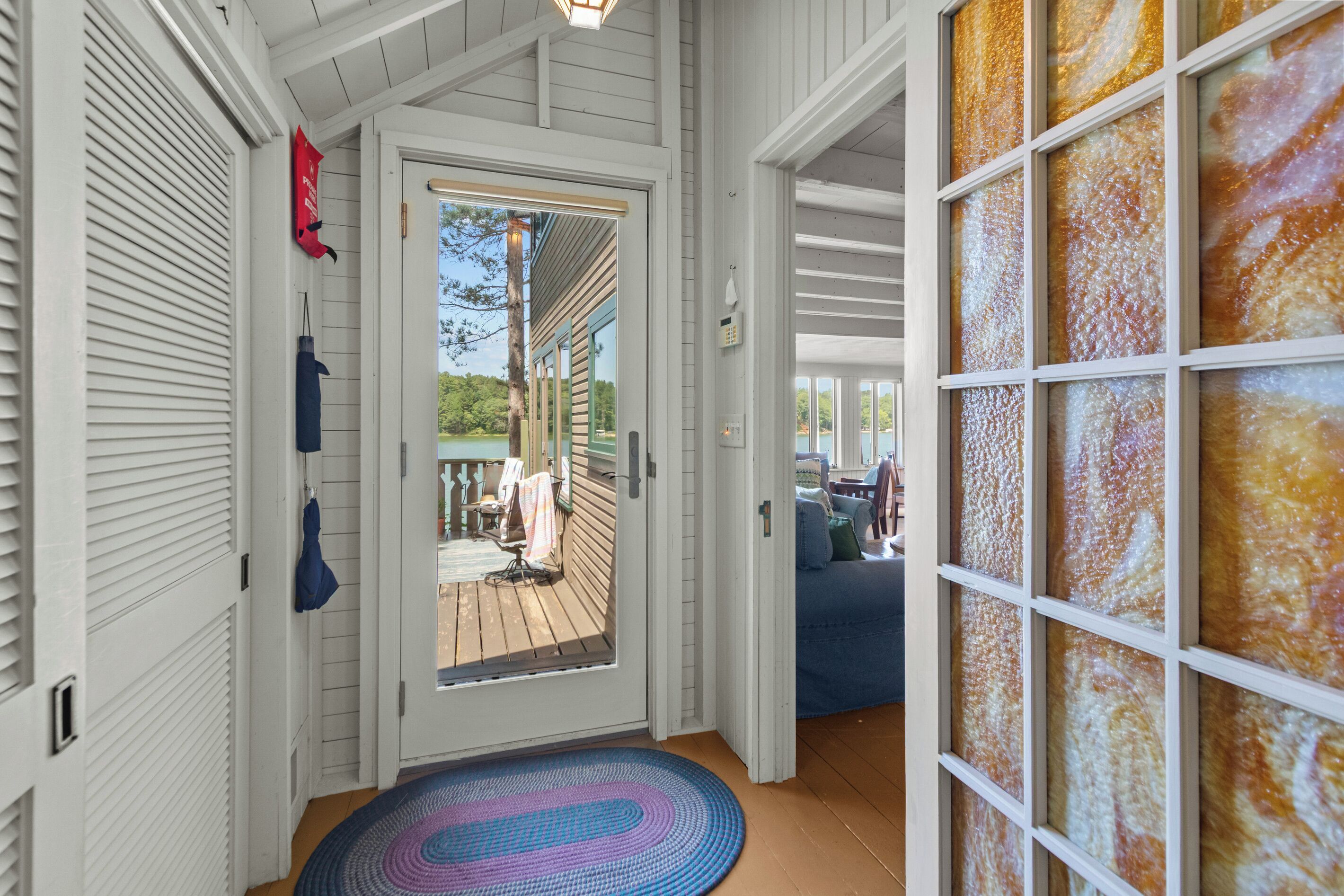A wooden interior with a door leading to an outdoor deck, a patterned rug, and a wall with a textured glass panel.