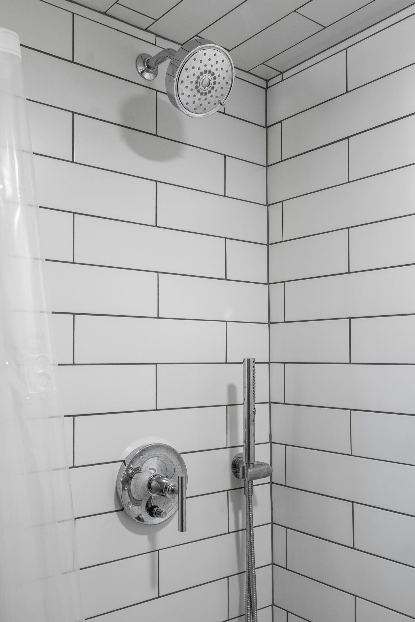 A shower with a handheld showerhead and a wall-mounted faucet in a corner with white tiled walls.