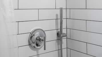 A shower with a handheld showerhead and a wall-mounted faucet in a corner with white tiled walls.